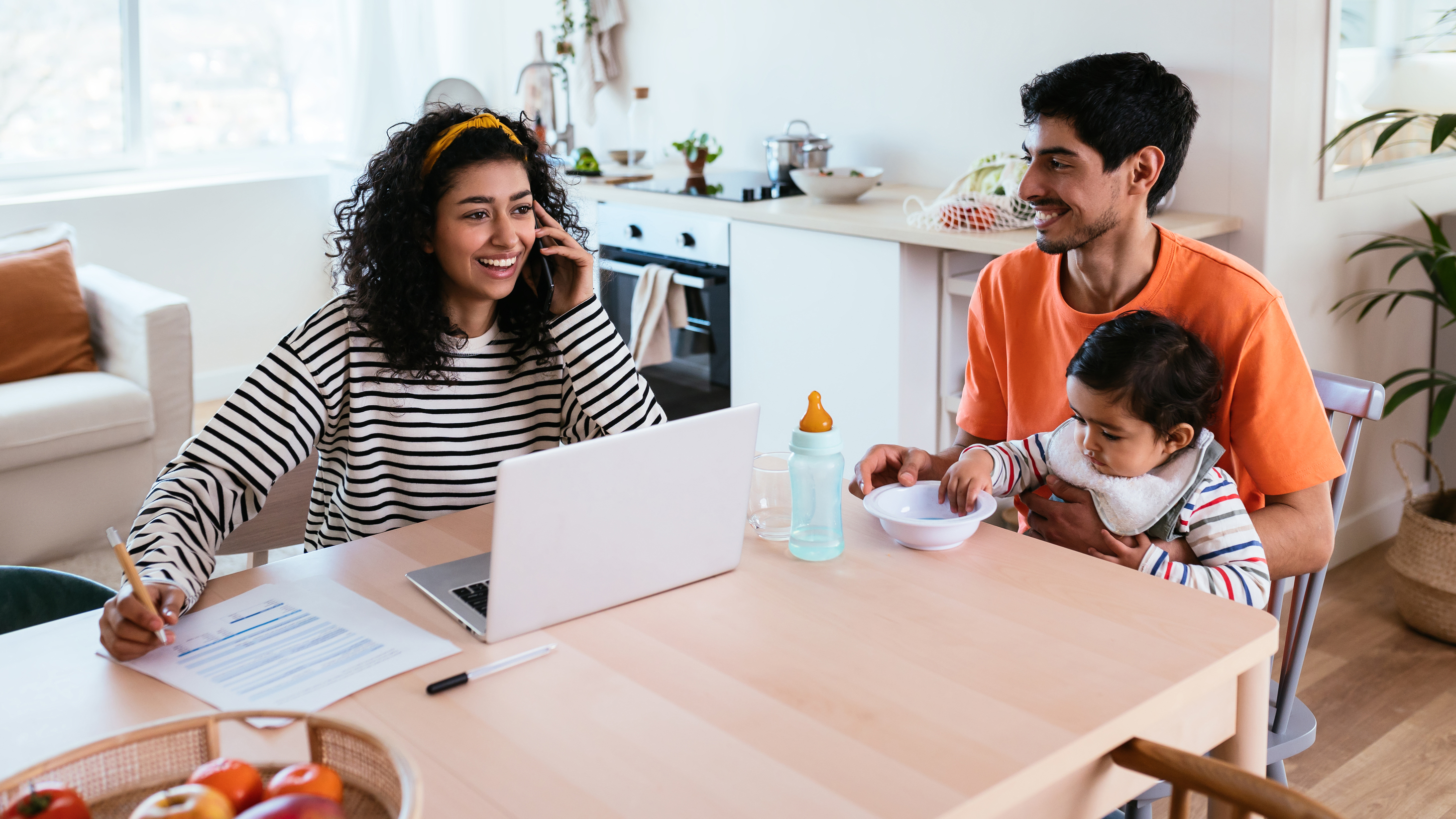 <p>Mom working on laptop, dad feeding baby.</p>